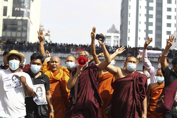 Buddhist monks flash the three-fingered salute as one monk addresses the crowd with a loudspeaker as they participate in a protest march in Yangon, Myanmar on Monday, Feb. 8, 2021. Tension in the conf ...