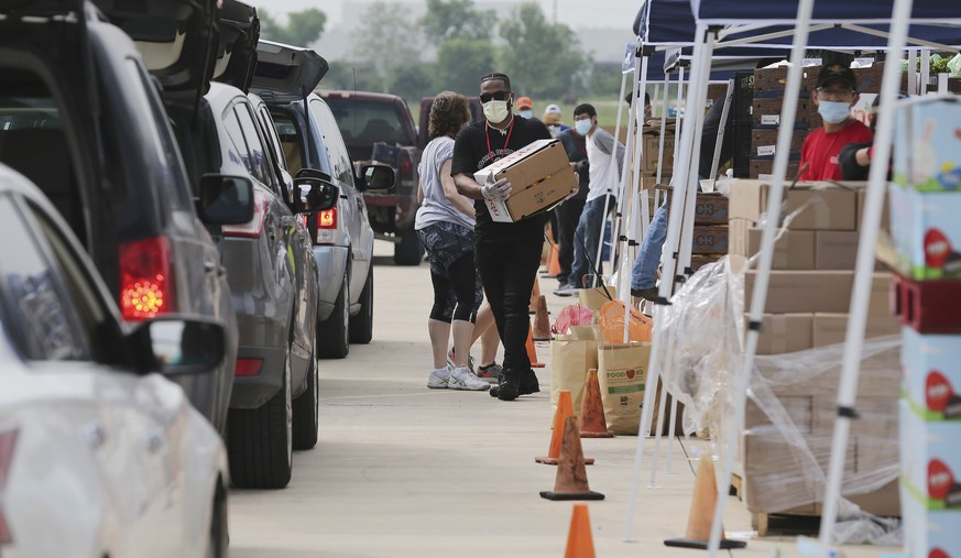 Helpers load food into cars as people in cars gather at Traders Village to get food from the San Antonio Food Bank on Thursday, April 9, 2020. The coronavirus pandemic has put enormous strain on house ...