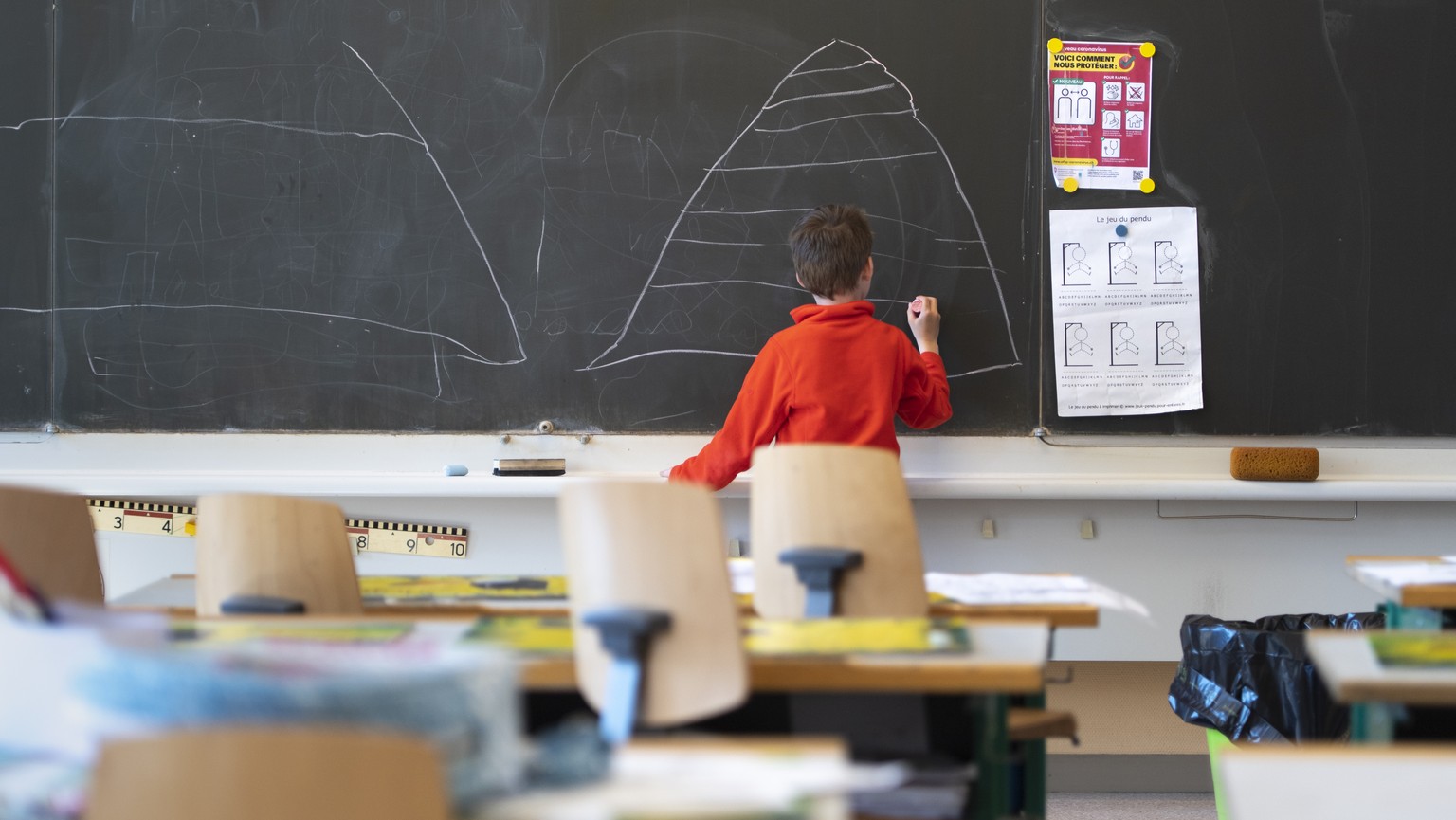 A child draws on the blackboard in an almost empty classroom as he attends a school childcare service at the school &quot;Etablissement primaire Pestalozzi &quot; during the state of emergency of the  ...