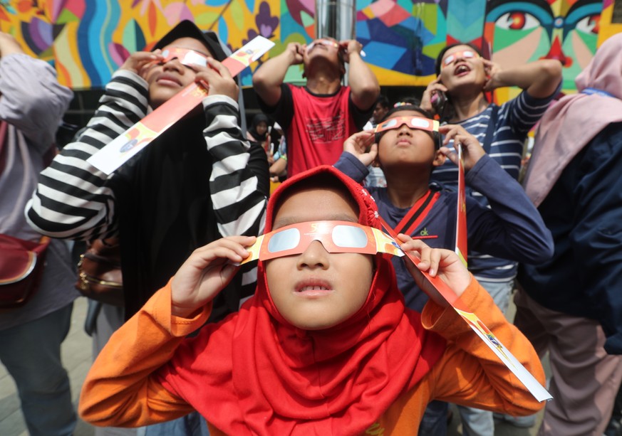 epa08090322 Indonesian kids wearing special glasses look up at the sun during a solar eclipse, outside the planetarium in Jakarta, Indonesia 26 December 2019. EPA/BAGUS INDAHONO
