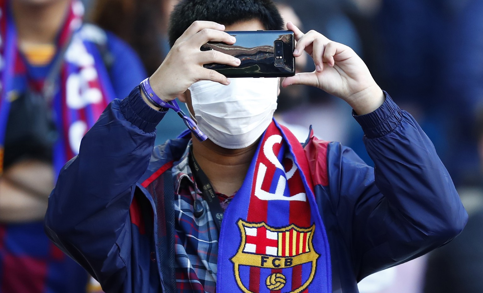 A Barcelona fan wears a face mask in an attempt to protect there self from the coronavirus uses his mobile prior a Spanish La Liga soccer match between Barcelona and Real Sociedad at the Camp Nou stad ...