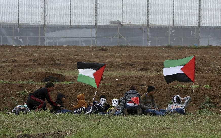 Protesters hid as they cover from teargas fired by Israeli troops near fence of Gaza Strip border with Israel, marking first anniversary of Gaza border protests east of Gaza City, Saturday, March 30,  ...