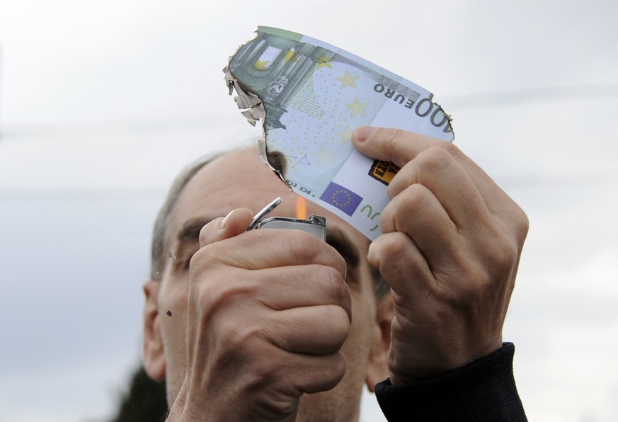 Ein Demonstrant in Athen zündet eine 100-Euro-Note an.