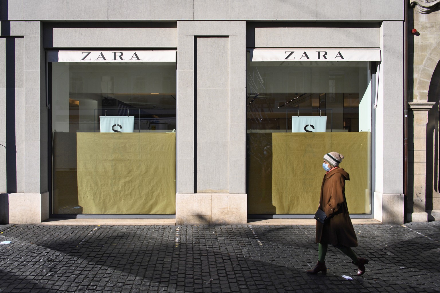 epa08945823 People wearing protective face masks walk in front of a closed Zara clothes shop during the first day of the closure of non-essential shops during the coronavirus disease (COVID-19) outbre ...