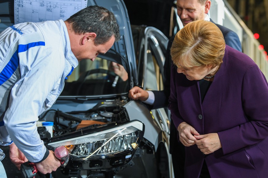 epa07971810 German Chancellor Angela Merkel (R) looks at the production process of a worker (L) next to Saxony State Premier Michael Kretschmer (R-covered) as she attends the Volkswagen ID.3 car assem ...