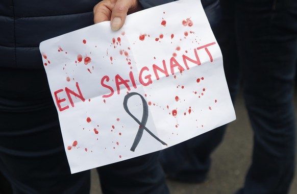 A person holds a poster reading &quot;Bleeding&quot;, playing with the French word for Teacher, outside the school where a slain history teacher was working, Saturday, Oct. 17, 2020 in Conflans-Sainte ...