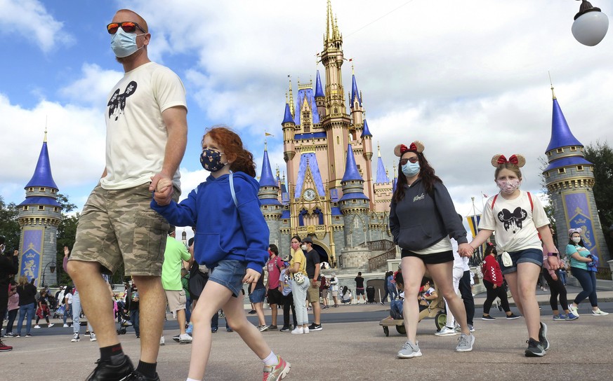 A masked family walks past Cinderella Castle in the Magic Kingdom, at Walt Disney World in Lake Buena Vista, Fla., Monday, Dec. 21, 2020. Disney&#039;s Florida parks are currently operating at 35% cap ...