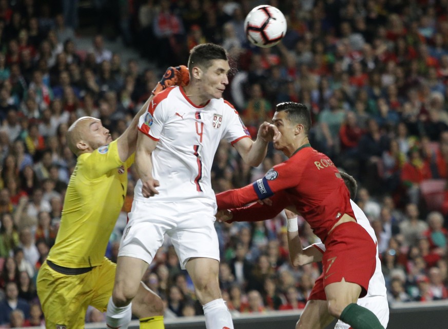 Serbia&#039;s goalkeeper Marko Dmitrovic, left, Serbia&#039;s Nikola Milenkovic, and Portugal&#039;s Cristiano Ronaldo challenge for the ball during the Euro 2020 group B qualifying soccer match betwe ...
