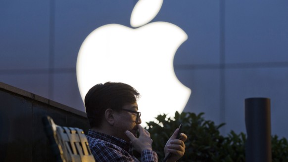 FILE - In this May 13, 2016 file photo, a man uses his mobile phone near an Apple store logo in Beijing, China. Apple Inc. has filed suit in China challenging Qualcomm Inc.’s fees for technology used  ...