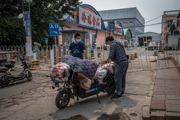 epa08482083 Men wearing protective face masks load a scooter with meat next next to the closed Xinfadi market building in Fengtai district, Beijing, China, 13 June 2020. One of Beijing&#039;s largest  ...