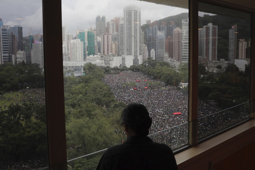 A person stands near a window overlooking a protest on Victoria Park in Hong Kong on Sunday, Aug. 18, 2019. Thousands of people streamed into a park in central Hong Kong on Sunday for what organizers  ...