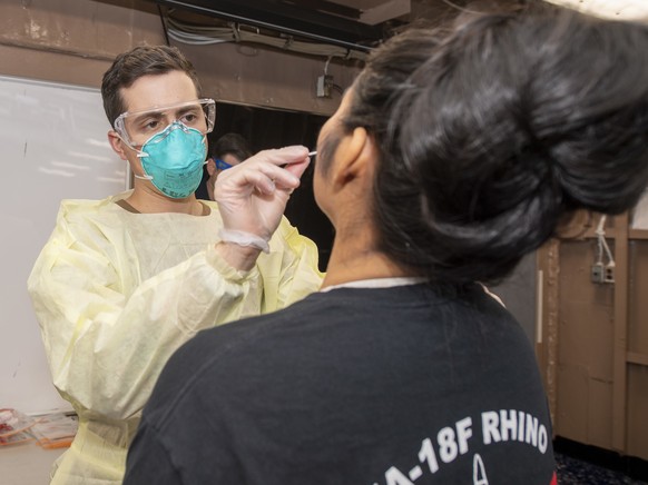 epa08341537 A handout photo made available by the US Navy shows medical staff taking a swab sample for COVID-19 testing aboard the aircraft carrier USS Theodore Roosevelt (CVN 71), at Apra Harbor, Gua ...