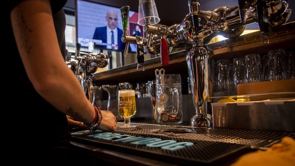 epa08892099 Bar staff pours a beer while watching Swiss Interior and Health Minister Alain Berset on a TV screen as he speaks during a press conference in Bern announcing new measures against the Coro ...