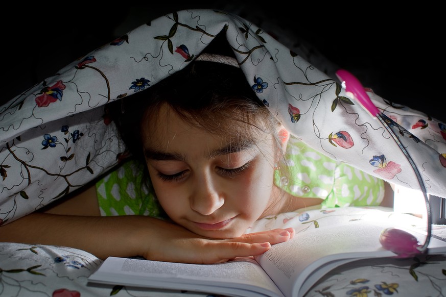 Mädchen liest unter der Bettdecke im Dunklen (Symbolbild)