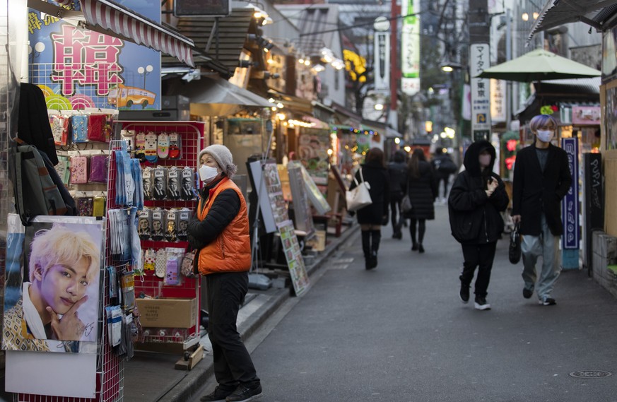 A sales person wearing a face mask stands outside as people walk on a street in a neighborhood dubbed &quot;Korea Town&quot; where businesses from Asian countries mainly from South Korea are situated  ...