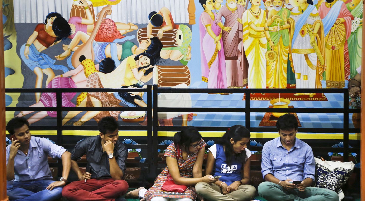 Young Buddhist devotees use their mobile phones as they sit under the frescos for prayer inside a temple during Buddha Purnima in Kolkata, India, Saturday, May 21, 2016. The festival marks the triple  ...