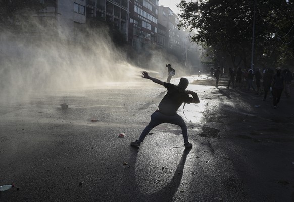 An anti-government protester prepares to throw a stone at a police water cannon vehicle in Santiago, Chile, Wednesday, Oct. 30, 2019. Chilean President Sebastián Pinera cancelled two major internation ...
