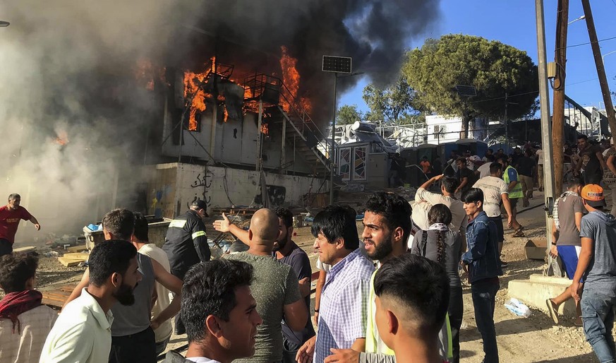 Migrants and refugees stand next to burning house containers at the Moria refugee camp, on the northeastern Aegean island of Lesbos, Greece, Sunday, Sept. 29, 2019. Migrants protesting at an overcrowd ...