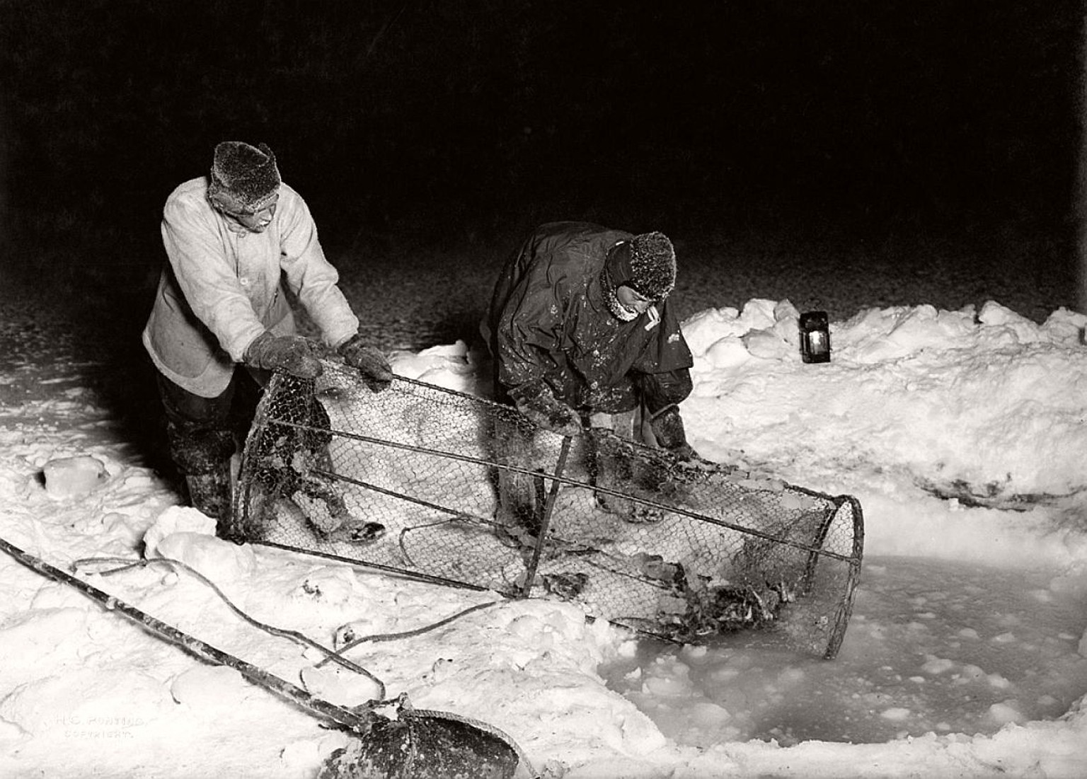 Koch Thomas Clissold und Arzt Edward Atkinson ziehen in der Winterdunkelheit der Antarktis eine mit Robbenködern besetzte Fischfalle hoch.