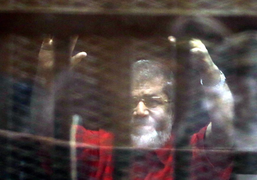 epaselect epa05292960 Ousted Egyptian President Mohamed Morsi raises his hand during a trial session on charges of espionage, Cairo, Egypt, 07 May 2016. Reports state a Cairo court sentenced six defen ...