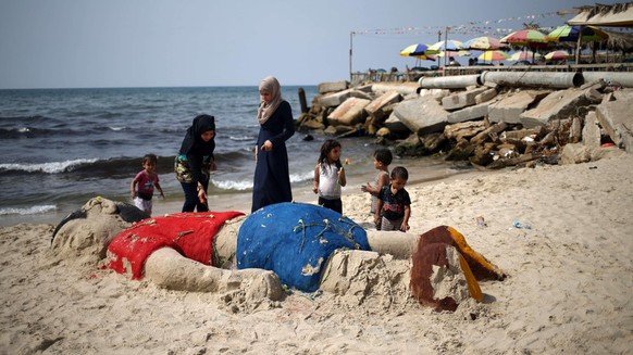 Palestinian girls put flowers on a sand sculpture depicting Syrian boy Aylan Kurdi, a three-year-old boy who drowned off Turkey, on September 7, 2015, on Gaza city beach. The sand sculpture replicates ...