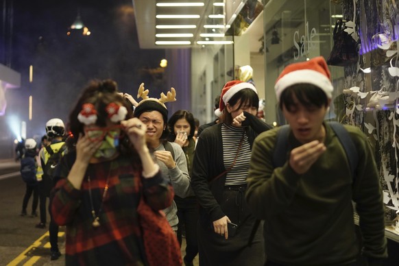 Residents dressed for Christmas festivities react to tear gas as police confront protesters on Christmas Eve in Hong Kong on Tuesday, Dec. 24, 2019. More than six months of protests have beset the cit ...