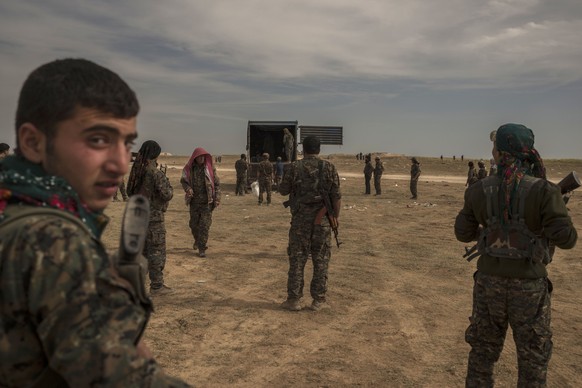 In this Sunday, March 10, 2019 photo, U.S.-backed Syrian forces stand guard as civilians wounded by airstrikes, during an offensive on the last area held by Islamic State group extremists, arrive by t ...