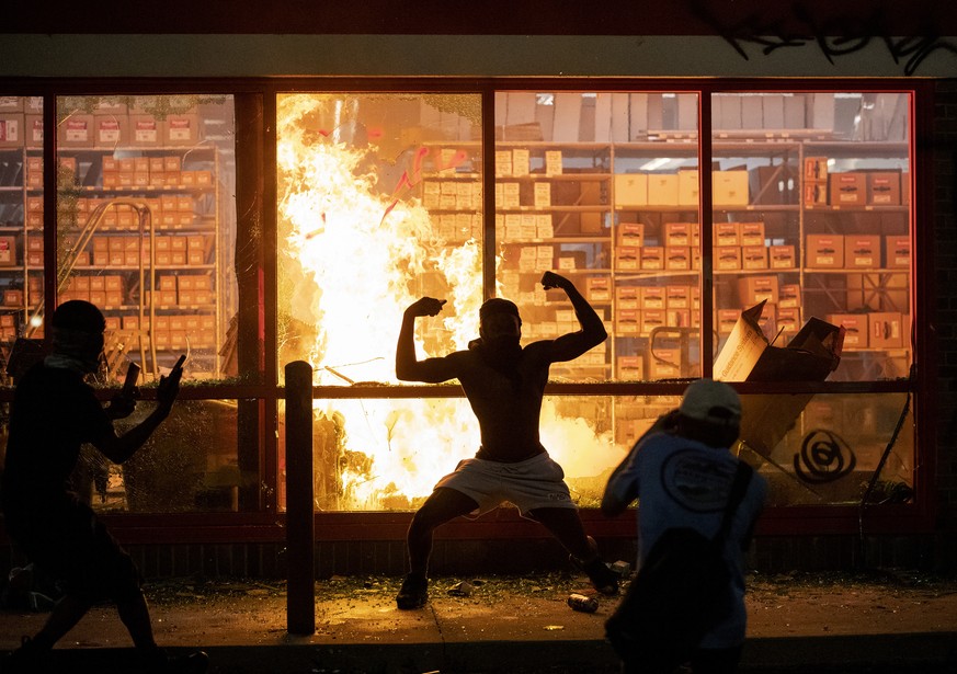 A man poses for photos in front of a fire at an AutoZone store, while protesters hold a rally for George Floyd in Minneapolis on Wednesday, May 27, 2020. Violent protests over the death of the black m ...