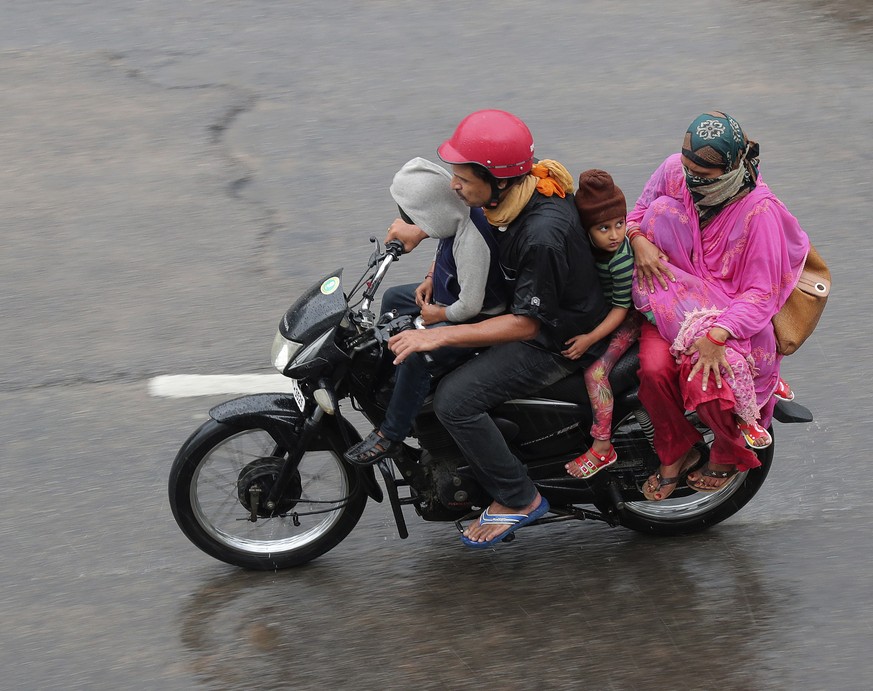 An Indian family rides a motorcycle in the rain in Hyderabad, India, Saturday, July 11, 2020. India receives its monsoon rains from June to September. (AP Photo/Mahesh Kumar A.)