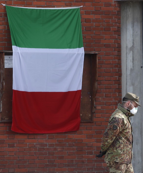 An Italian flag hangs outside the San Giuseppe church as an Army soldier walks past trucks waiting to load coffins to be taken to crematoriums in Venice and Udine, from Seriate, near Bergamo, northern ...