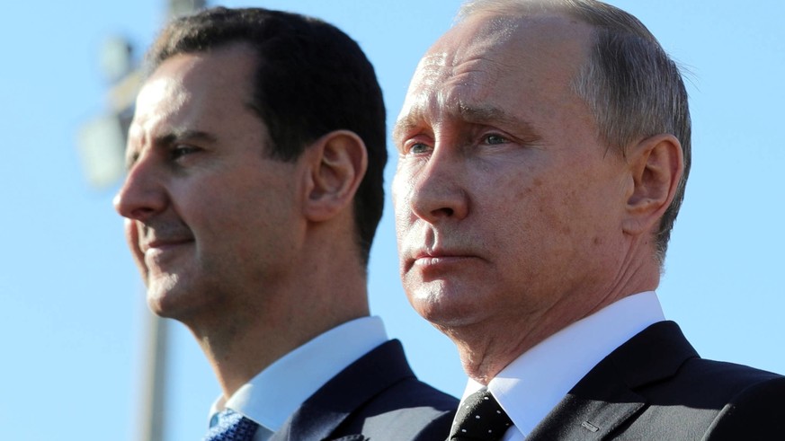 FILE - This Dec. 11, 2017 file photo, shows Russian President Vladimir Putin, right, and Syrian President Bashar Assad watching troops march at the Hemeimeem air base in Syria. In comments published o ...
