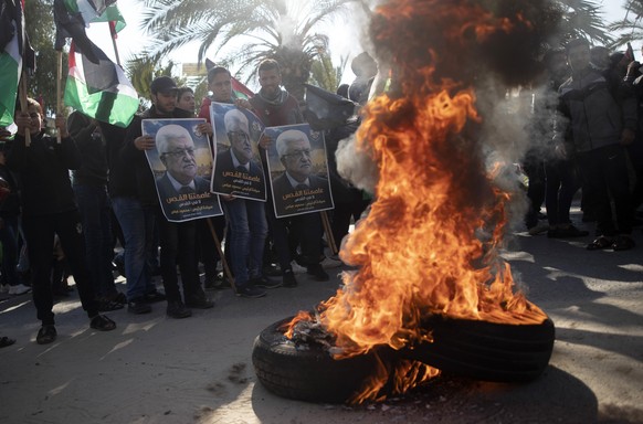 Palestinian protesters stand holding pictures of the Palestinian president, Mahmoud Abbas, in front of burning tires during a protest against the U.S. Mideast peace plan, in Gaza City, Monday, Jan. 28 ...
