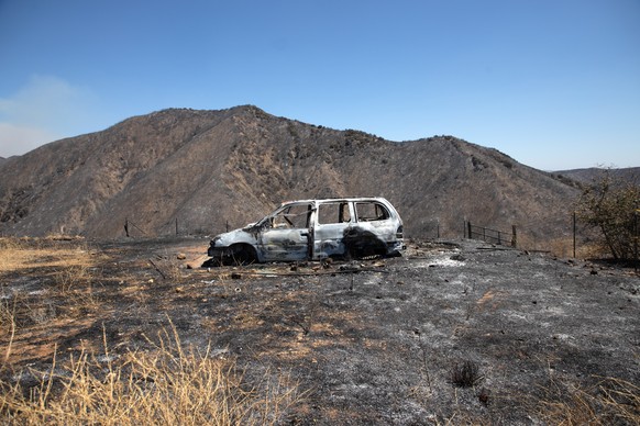 epa08581174 A burned out vehicle sits near a hill after the the Apple Fire past through the area, in Banning, California USA, 02 August 2020. The fire has burned more than 20,000 acres since it starte ...