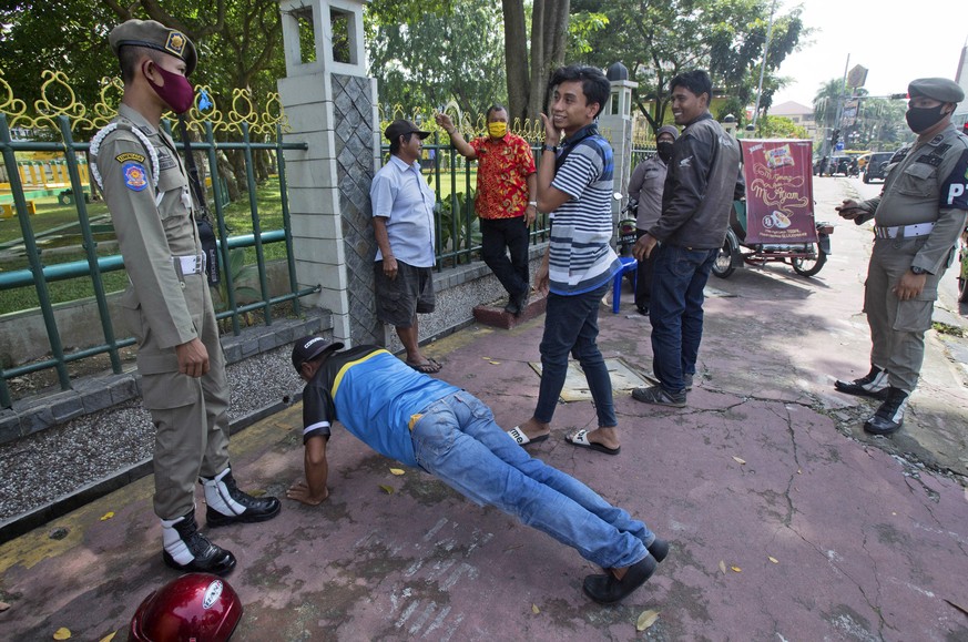 Public Order Agency officers penalize a man with push ups as others look on after they were caught violating city regulation requiring people to wear face mask in public places to curb the spread of t ...