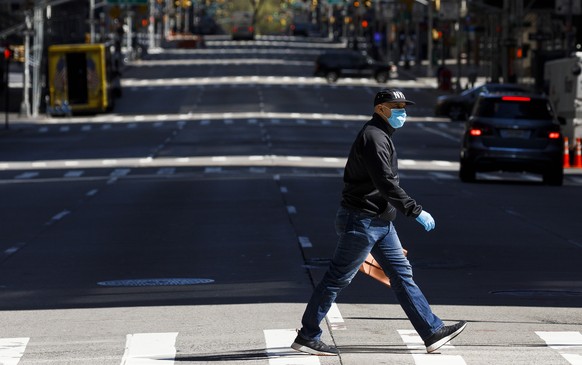 epa08364951 A man in a mask crosses 6th avenue in New York, New York, USA, 15 April 2020. New York Governor announced plans to issue an executive order that will require everyone to wear a mask or fac ...