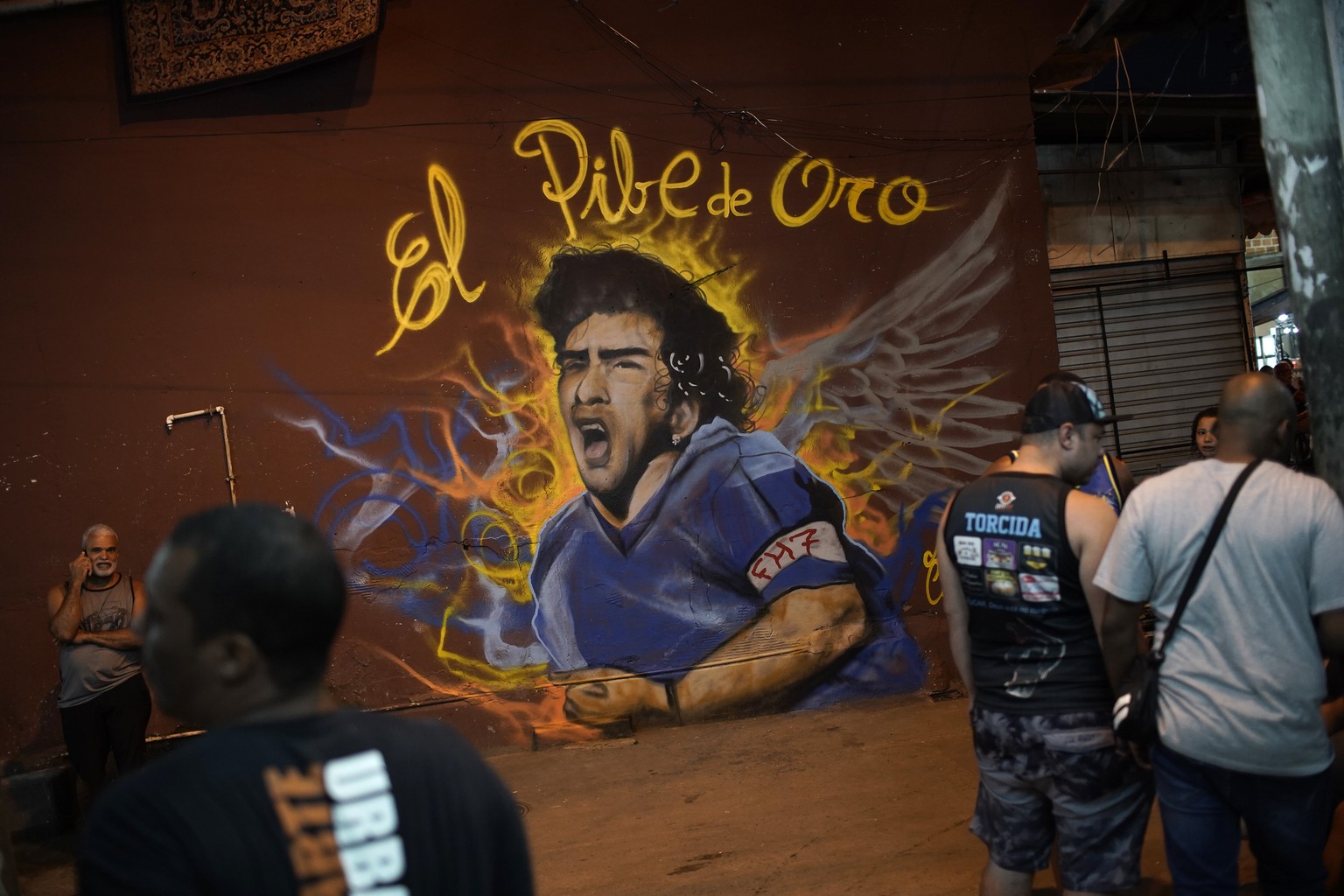 People stand next to a mural made by graffiti artist Angelo Campos in honor of late Argentina&#039;s soccer legend Diego Maradona at a favela in Rio de Janeiro, Brazil, Wednesday, Nov. 25, 2020. The D ...