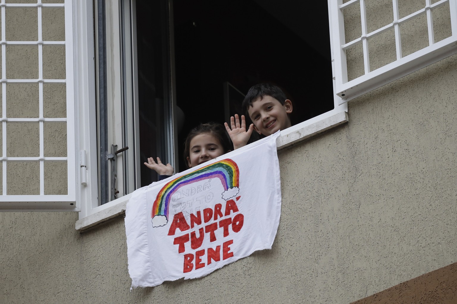 In this photo taken on Friday, March 13, 2020, Francesco and Greta Innominati wave after placing a banner reading &quot;Everything is gone be all right&quot; out of a window of their apartment in Rome ...