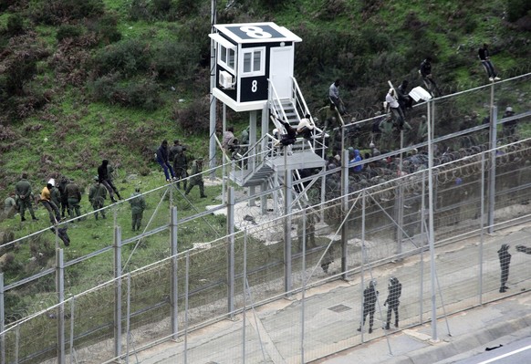 epa05667103 Moroccan Police look at immigrants trying to jump the six-meter-high fence in Ceuta, Spanish enclave on the north of Africa, 09 December 2016. More than 250 immigrants managed to jump the  ...