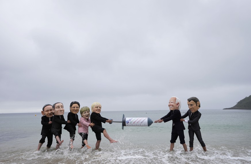 Activists wearing giant heads of the G7 leaders tussle over a giant COVID-19 vaccine syringe during an action of NGO&#039;s on Swanpool Beach in Falmouth, Cornwall, England, Friday, June 11, 2021. Lea ...