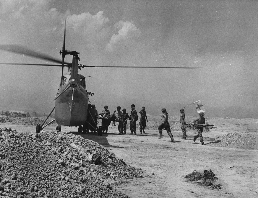 A Red Cross flag is held aloft as a wounded French Union soldier is placed on a helicopter for evacuation from front line fighting against Communist-led Viet Minh troops at Dien Bien Phu, Indochina, M ...