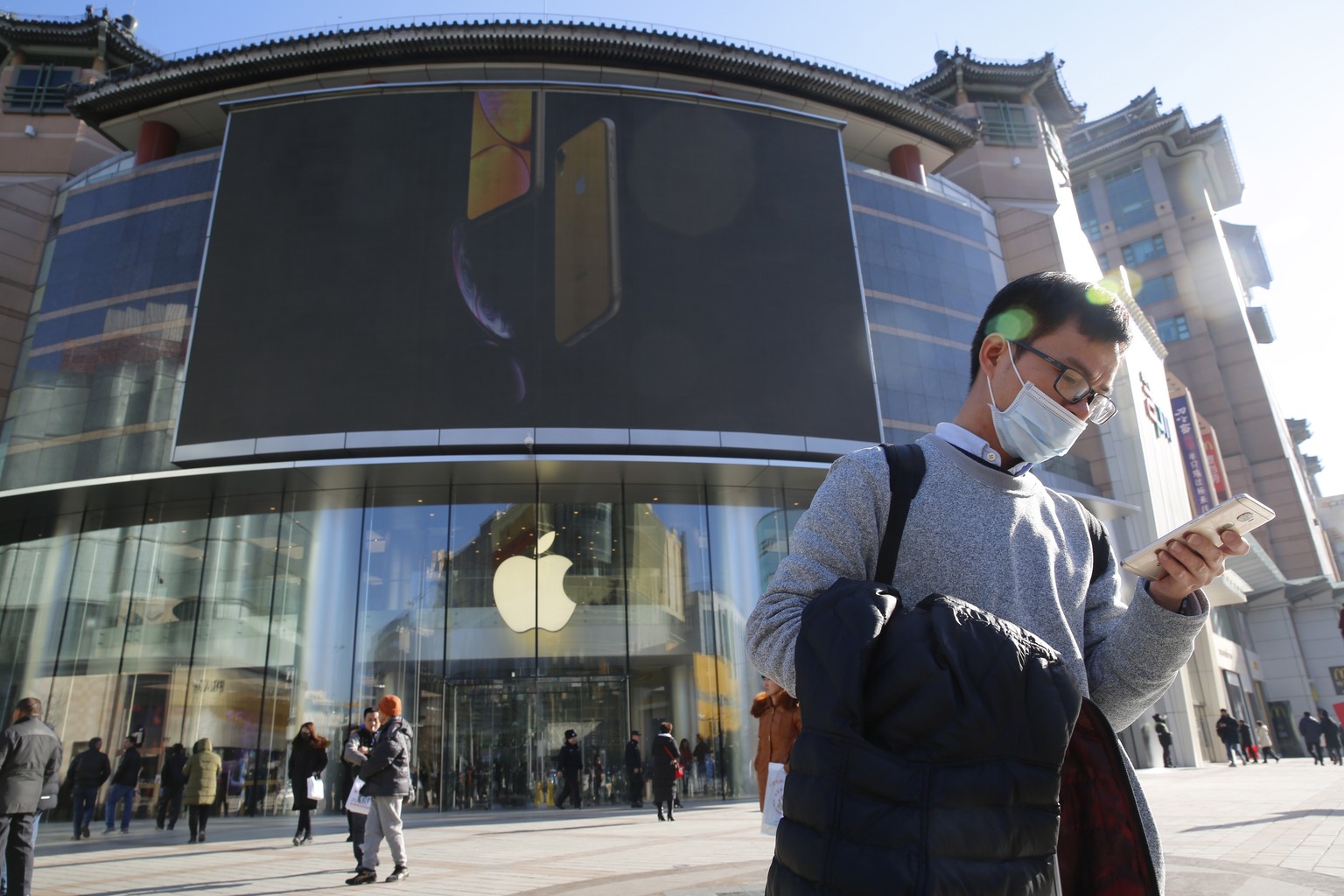 epa07259019 (FILE) - A Chinese man uses his mobile phone outside an Apple store while an iPhone XR picture is displayed on a large screen in Beijing, China, 12 December 2018 (reissued 03 January 2019) ...