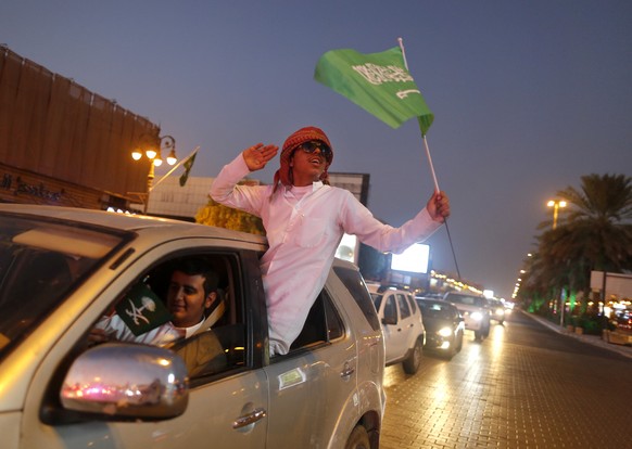 A Saudi waves a national flag as he hangs out the window of a car during celebrations marking National Day to commemorate the unification of the country as the Kingdom of Saudi Arabia, in Riyadh, Saud ...
