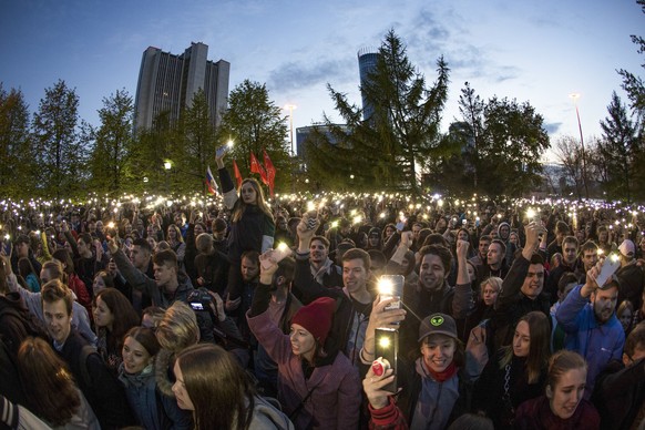 Demonstrators wave their cell phones as they gather in front of a new built fence blocked by police, during a protest against plans to construct a cathedral in a park in Yekaterinburg, Russia, Wednesd ...