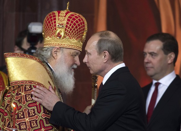 FILE - In this Sunday, May 5, 2013 file photo Russian Orthodox Patriarch Kirill, left, greets Russian President Vladimir Putin, with Prime Minister Dmitry Medvedev at right, during an Easter service i ...
