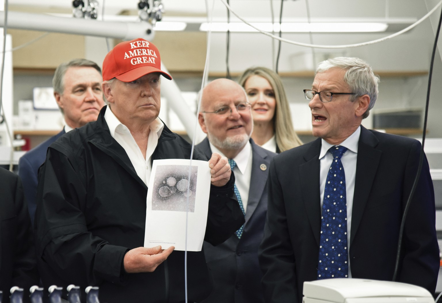 President Donald Trump holds a photograph of coronavirus as Dr. Steve Monroe,right, with CDC speaks to members of the press at the headquarters of the Centers for Disease Control and Prevention in Atl ...