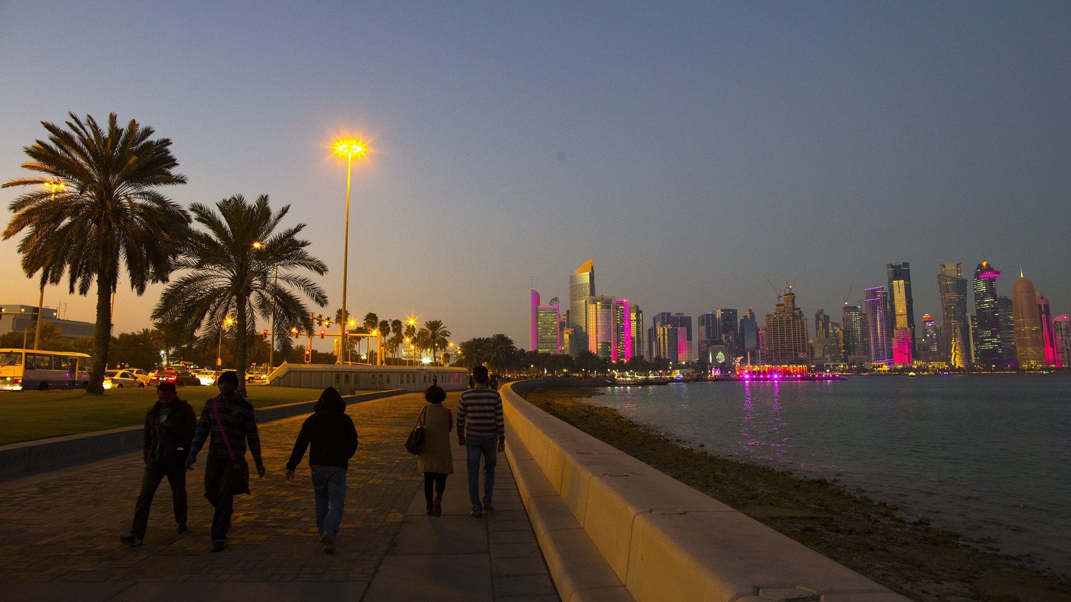 epa04591688 People walk on the corniche promenade in front of the skyline of Doha&#039;s West Bay high rise buildings at sunset, Doha, Qatar, 28 January 2015. The men&#039;s Handball World Championshi ...