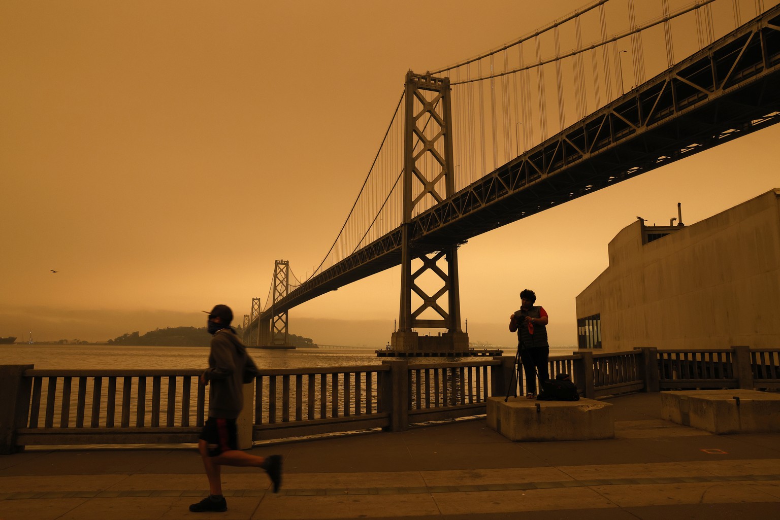 epa08657795 A view of the San Francisco Bay Bridge under an orange overcast sky in the afternoon in San Francisco, California, USA, 09 September 2020. California wildfire smoke high in the atmosphere  ...