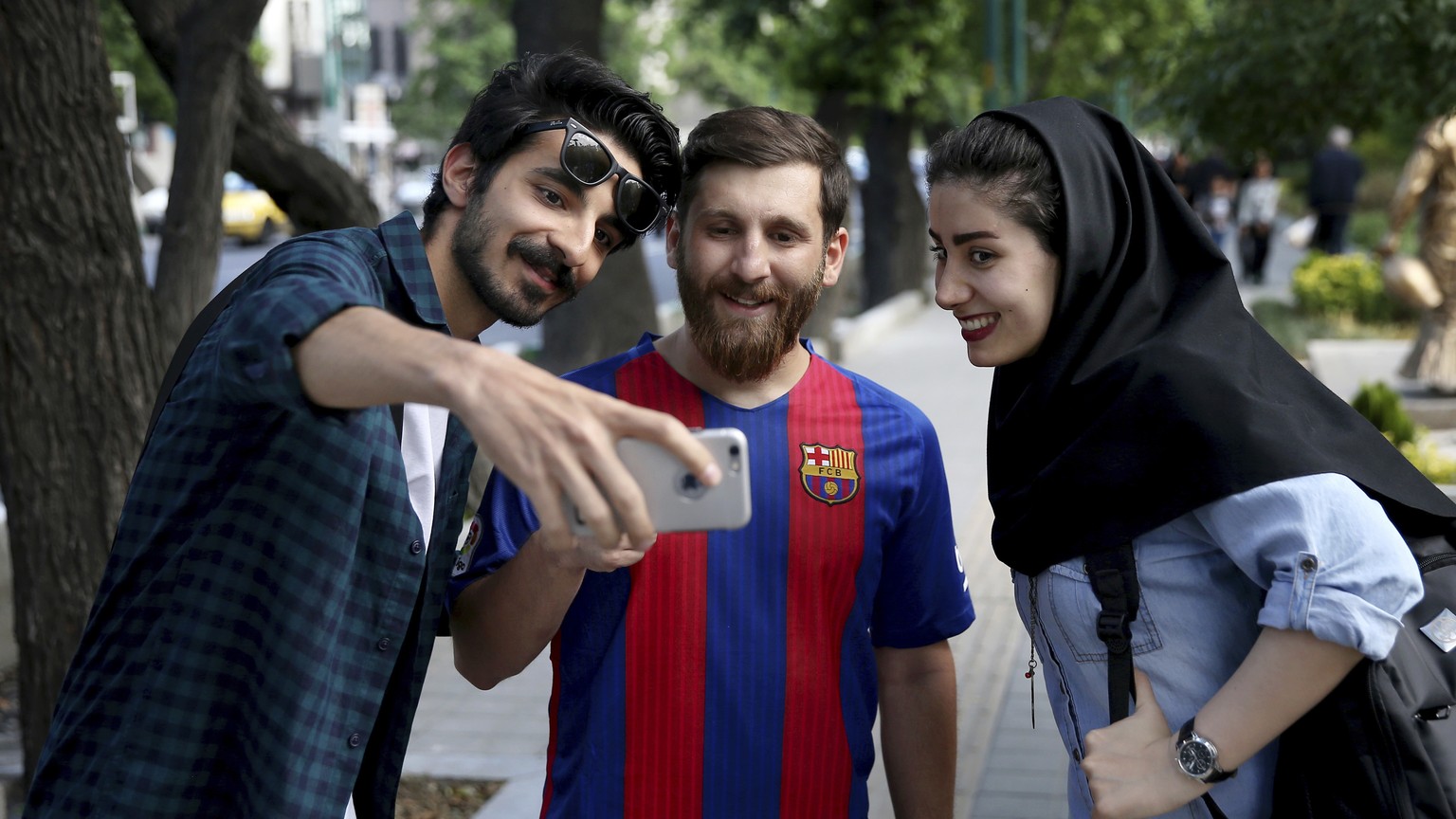 In this Monday, May 8, 2017 photo, two Iranians take a selfie with Reza Parastesh, Iranian doppelganger, or look-alike, of Lionel Messi, Argentinian soccer legend in Tehran, Iran. (AP Photo/Ebrahim No ...