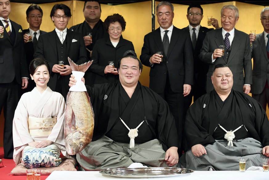 Newly promoted Japanese sumo wrestler Kisenosato, center, accompanied by his stable master Tagonoura, right, and the master&#039;s wife, Kotomi, holds up a red sea bream during a formal ceremony to no ...