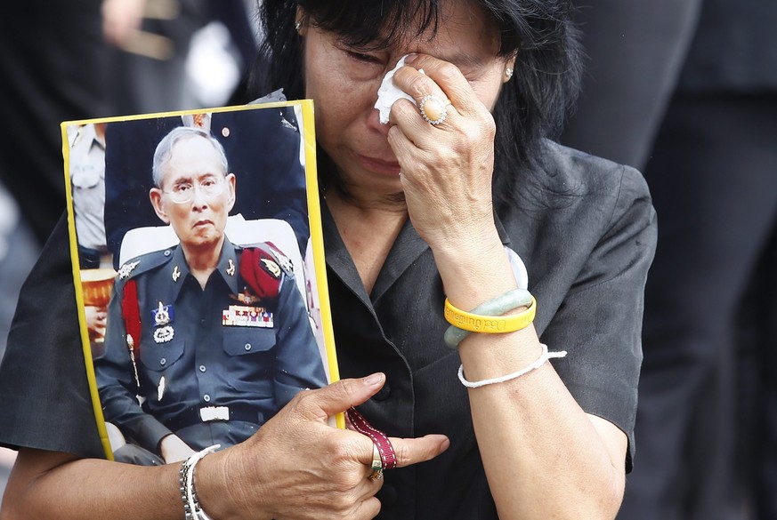 epa05597359 A Thai mourner holds a portrait of late Thai King Bhumibol Adulyadej as she takes part in a mass royal anthem singing to honor the late Thai King Bhumibol Adulyadej at Sanam Luang (Royal F ...